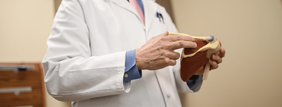 A surgeon holding a model of a shoulder joint.